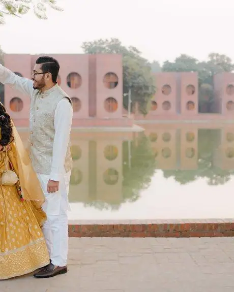 The couple run hand in hand across a wide, empty road lined with trees, the bride in yellow and the groom in white.