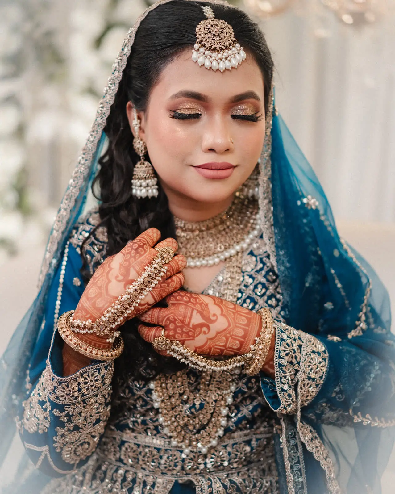 Portrait of Anika in blue and silver, hands folded, mehndi visible