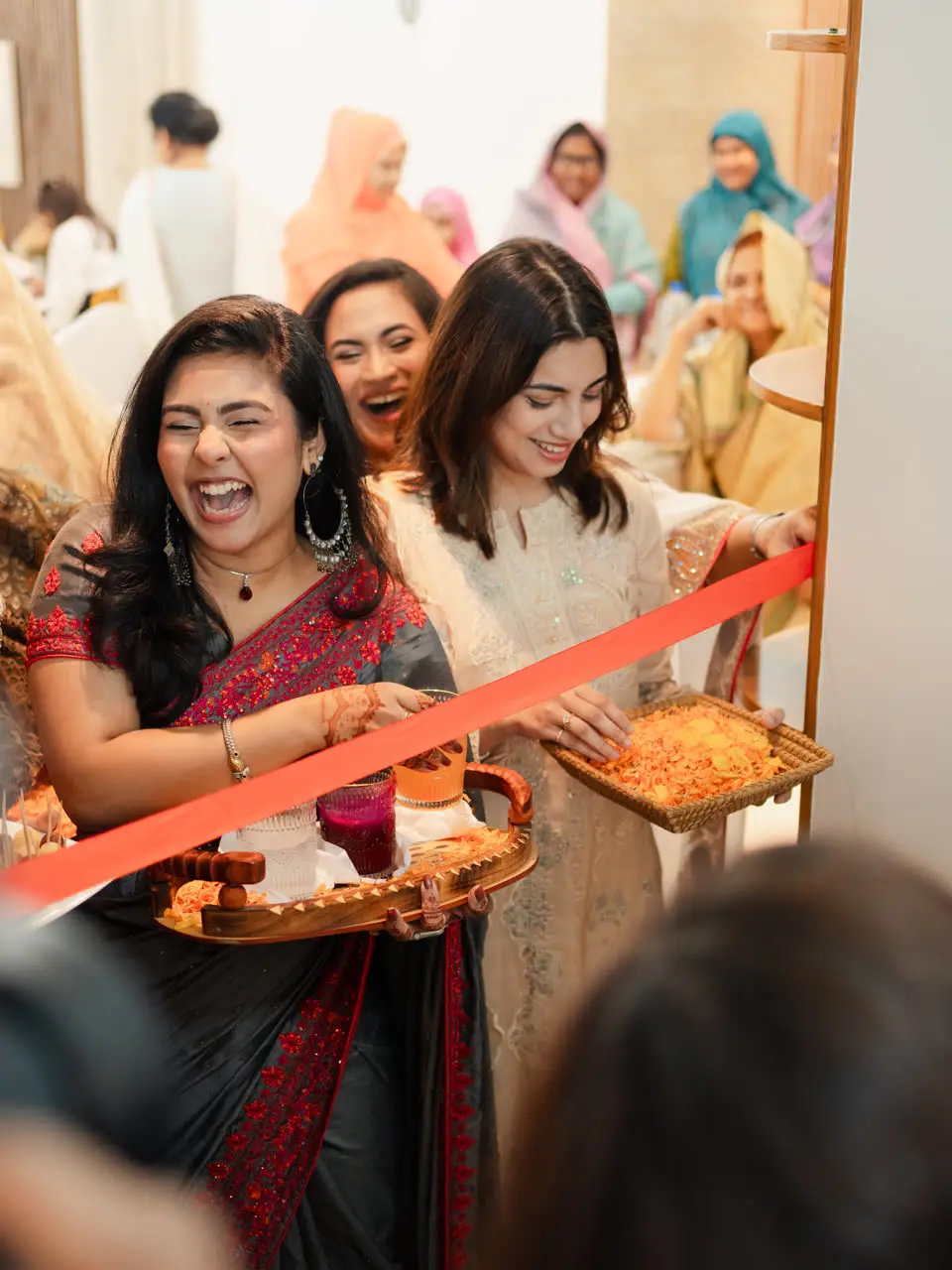 The bride’s cousins laugh as they block the doorway with a red ribbon for the groom’s arrival