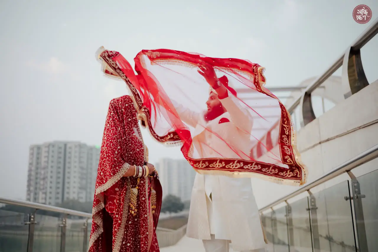 Nadia’s red veil caught by the wind on a rooftop