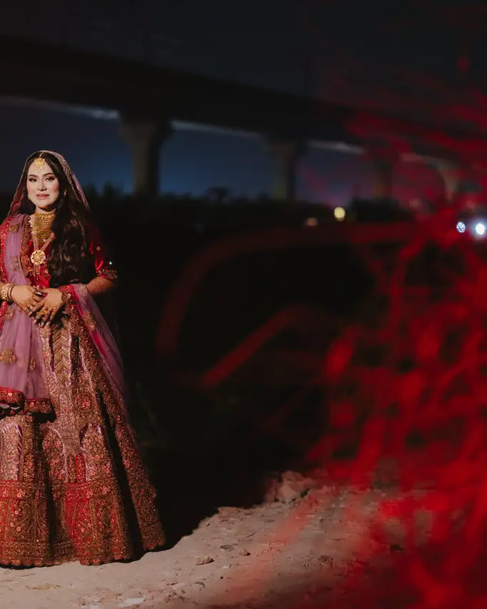 Nadia in a red bridal lehenga at night, a blur of red light beside her