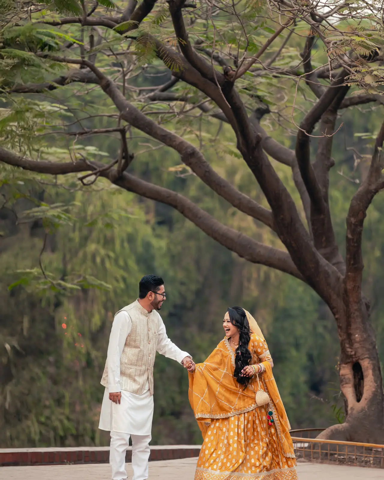 Nadia in a marigold saree leads Tanvir by the hand under a bare tree