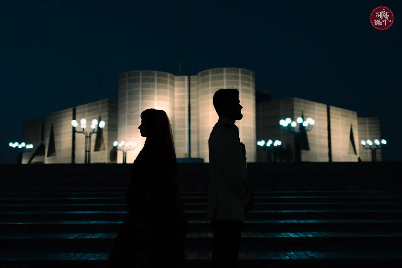 Two silhouettes in front of a lit monument at night
